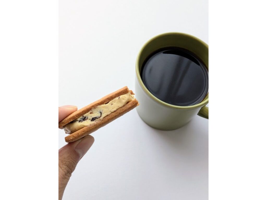 マルセイバターサンドを一口食べて手に持ち、コーヒーと一緒に撮影した写真