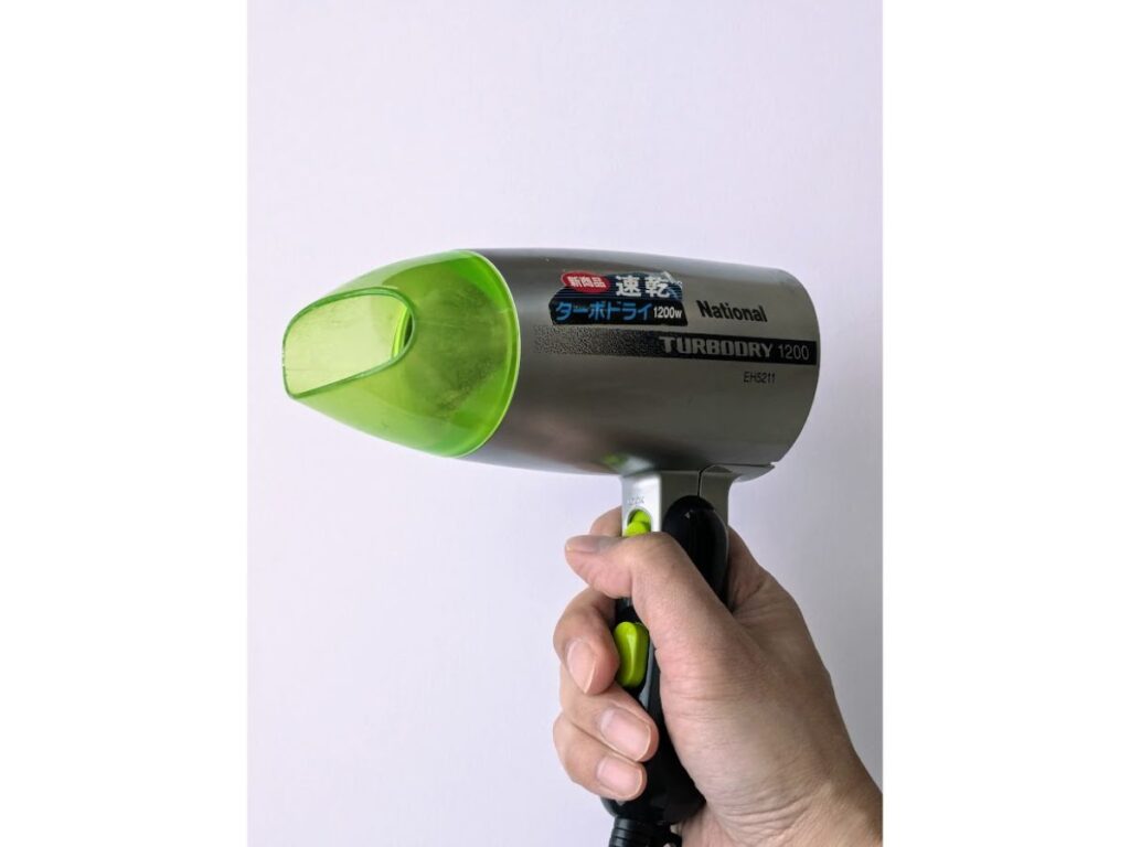 片手で持ったヘアドライヤーを正面から見た写真。透明感のある緑色の細い吹き出し口ノズルと、その奥にある網目状のパーツの様子。