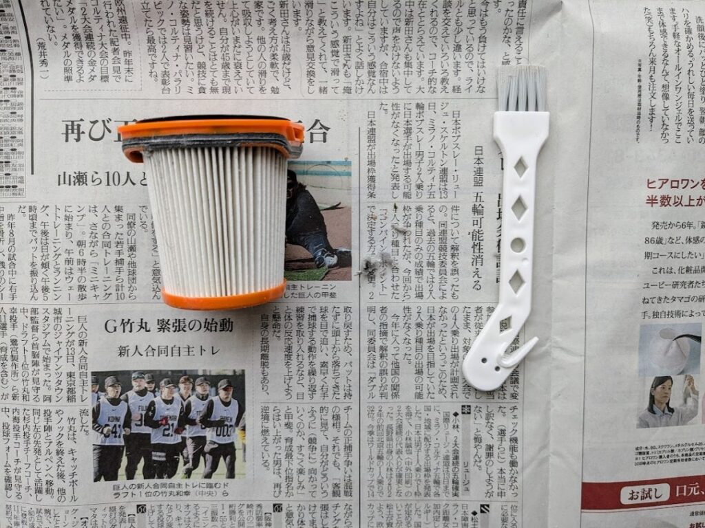 新聞紙の上に置いたシャーク掃除機のフィルターと掃除用ブラシ