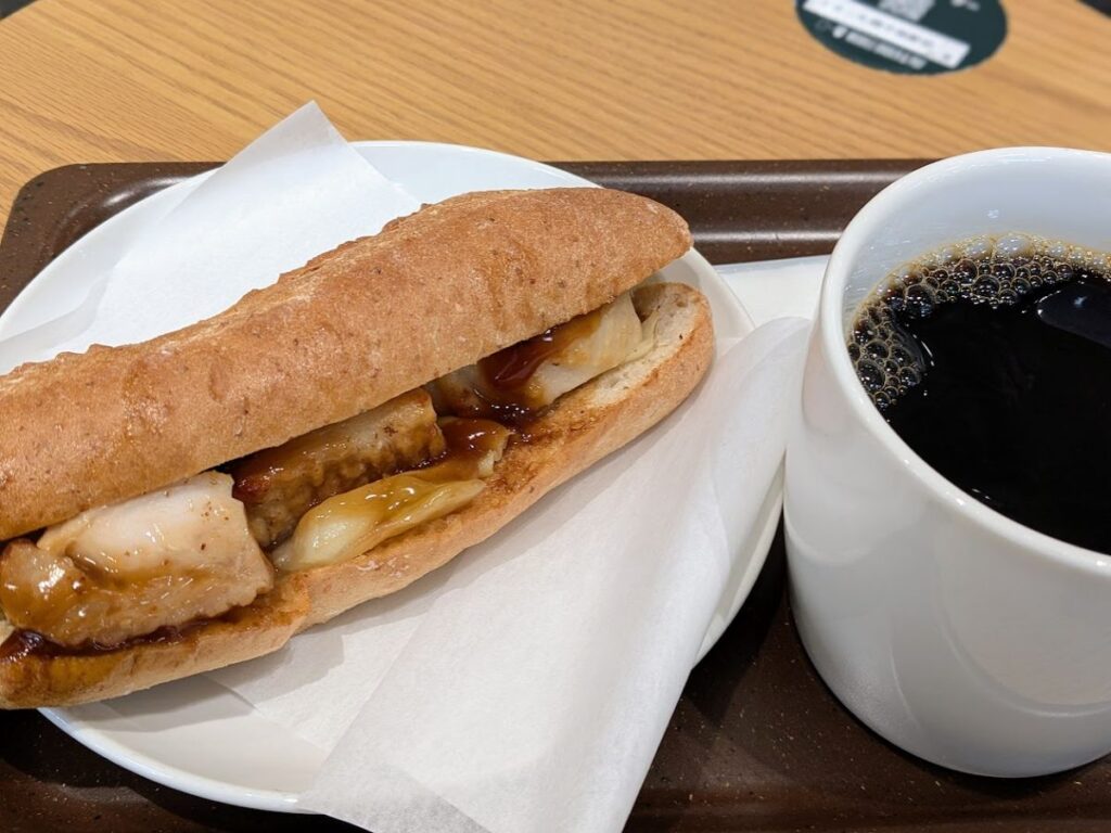 - スタバのフード（パンのサンド）とブリュードコーヒー（ブラック）をトレーに置いた写真。白いマグの表面に泡が見える






