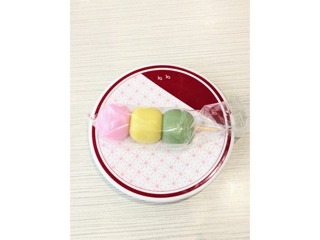 はま寿司の三色だんご(ピンク・黄色・緑)が個包装で串に刺さり、丸皿にのっている写真