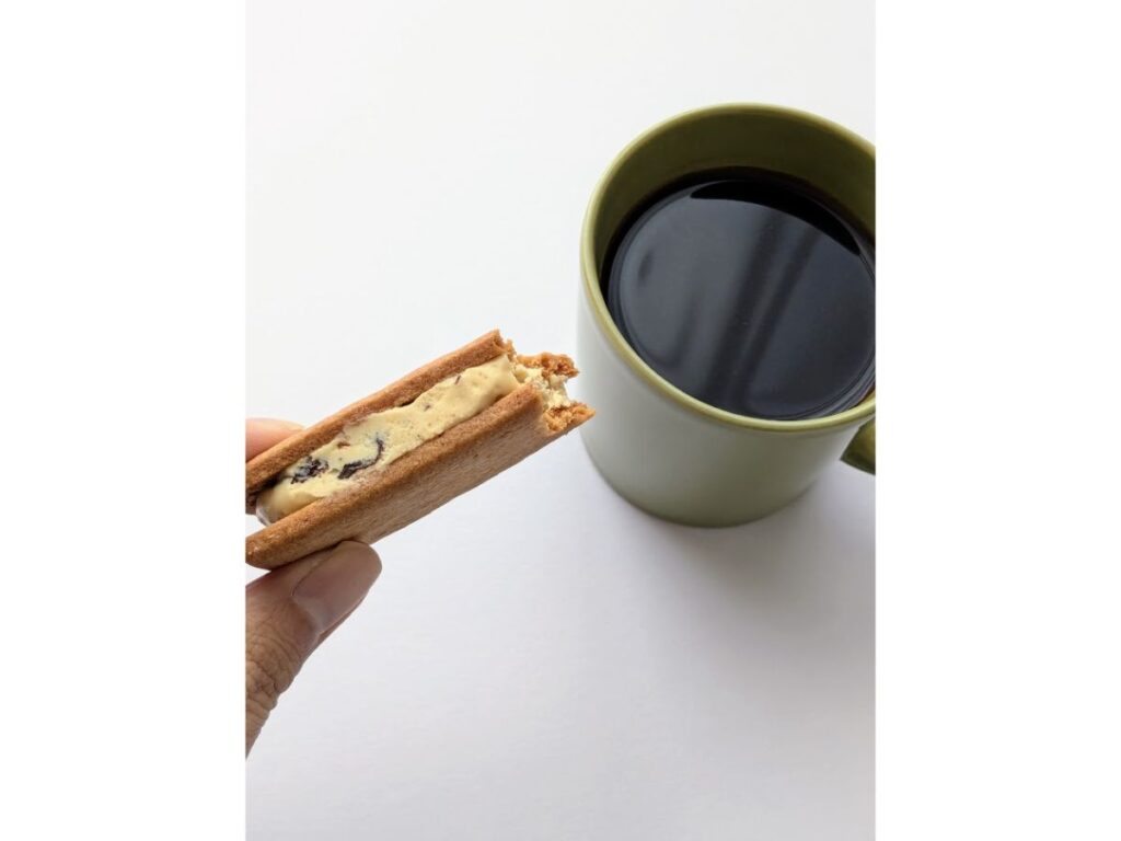 マルセイバターサンドを手に持ち、マグカップのブラックコーヒーと一緒に写した写真