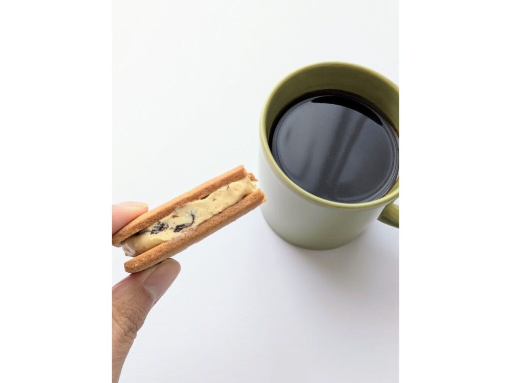 マルセイバターサンドを手に持ち、マグカップのブラックコーヒーと一緒に写した写真