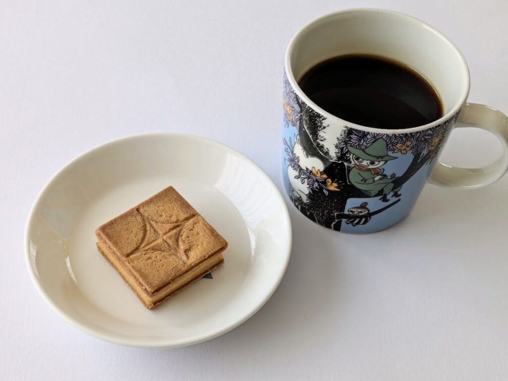 プレスバターサンドをイッタラの皿に載せ、アラビアのムーミンカップにコーヒーを入れた画像